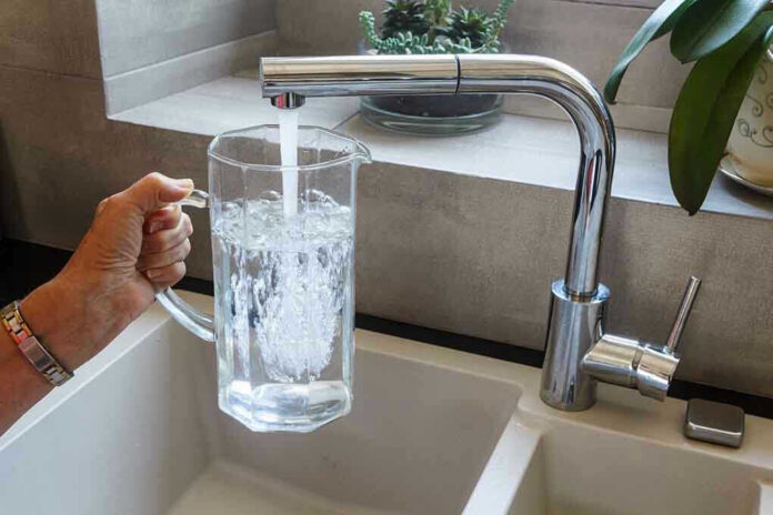 Hand filling pitcher with water from faucet.