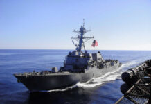 Warship with American flag sailing in the ocean.