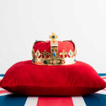 Royal Return — Without The Royal Job A royal crown resting on a red velvet pillow with a British flag background