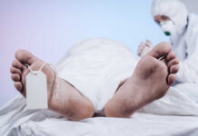 Covered body on morgue table with toe tag and person in protective gear