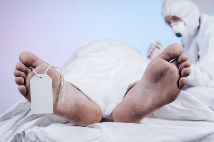 Two,Feet,Of,A,Dead,Body,,With,An,Identification,Tag Covered body on morgue table with toe tag and person in protective gear