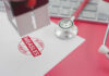 A stamp marking 'MEASLES ALERT' on a piece of paper next to a stethoscope and keyboard