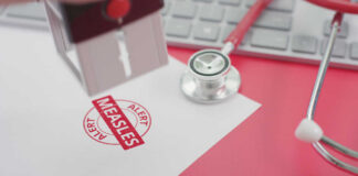 A stamp marking 'MEASLES ALERT' on a piece of paper next to a stethoscope and keyboard