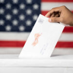 Barcode Ballots Ignite Federal Showdown Hand inserting mail-in ballot envelope into ballot box