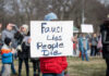 Shredded Emails Rock Fauci’s Inner Circle Person holding sign reading Fauci Lies, People Die.