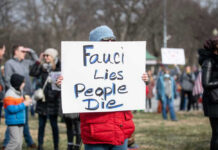 Person holding sign reading Fauci Lies, People Die.