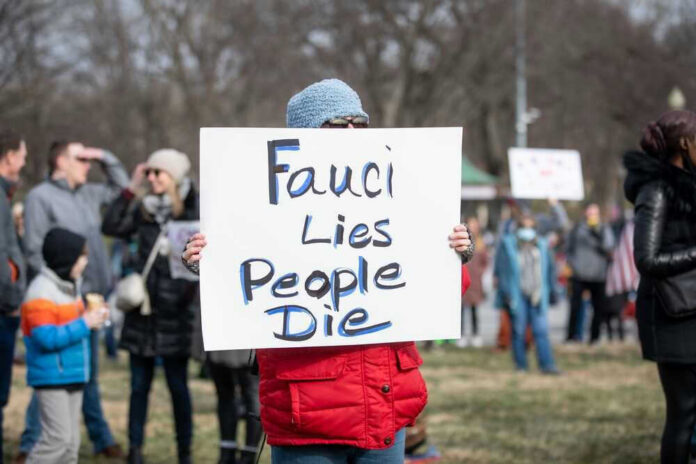 shutterstock_2115278627 Person holding sign reading Fauci Lies, People Die.