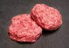 Two raw ground meat patties on a dark surface
