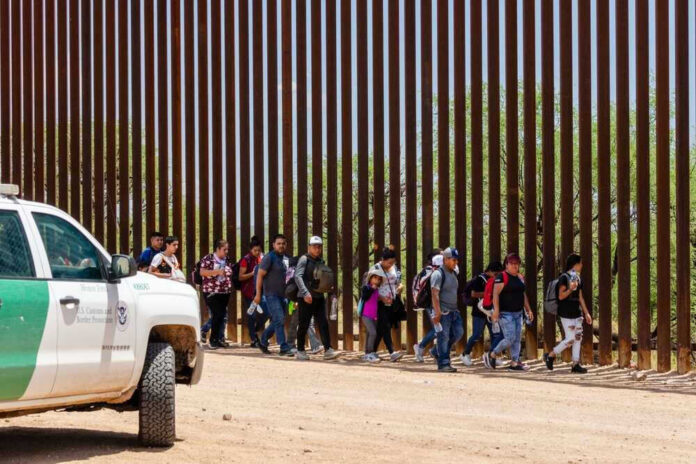 shutterstock_2333258557-1 Group of people walking by a border fence.