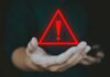 Big Tech Dragged Into Court Over Teen Deaths A hand holding a red warning triangle with an exclamation mark