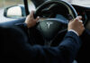 Belt Fail Risk Triggers Massive Recall Person driving a Tesla car steering wheel