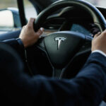Belt Fail Risk Triggers Massive Recall Person driving a Tesla car steering wheel