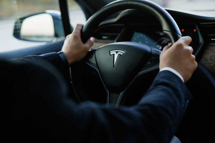 shutterstock_2474065113 Person driving a Tesla car steering wheel