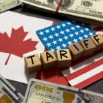 Wooden blocks spelling tariffs on U.S. and Canadian flags with dollar bills