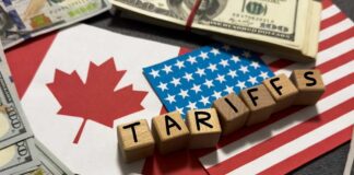 Wooden blocks spelling tariffs on U.S. and Canadian flags with dollar bills