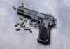 Black semi-automatic pistol with scattered brass cartridges on a gray surface