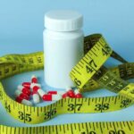 A white pill bottle surrounded by red and white capsules and a yellow measuring tape