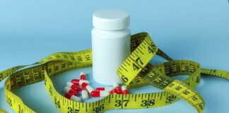 A white pill bottle surrounded by red and white capsules and a yellow measuring tape