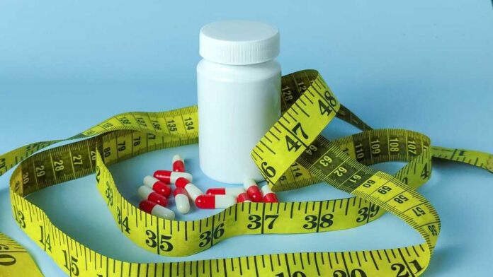 White,Pill,Bottle,With,Capsules,And,Yellow,Measuring,Tape,Representing A white pill bottle surrounded by red and white capsules and a yellow measuring tape