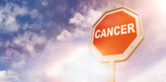 A stop sign with the word 'CANCER' against a cloudy sky