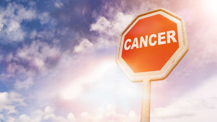 Cancer,,Text,On,Red,Traffic,Stop,Sign,In,Front,Of A stop sign with the word 'CANCER' against a cloudy sky