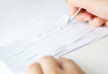 Record Paychecks, But What’s Missing? Person signing a check on a white background.