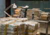 Narco-Terror Bombshell Lands In U.S. Stacks of wrapped packages in a dimly lit warehouse