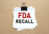 ALERT: Tainted Food Triggers FDA Action A notice labeled 'FDA RECALL' clipped to white papers on a brown background