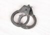 Toddler, Gun, Daycare – Cop Arrested A pair of metallic handcuffs resting on a light wooden surface