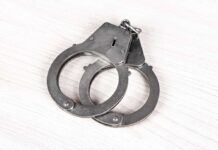 Toddler, Gun, Daycare – Cop Arrested A pair of metallic handcuffs resting on a light wooden surface