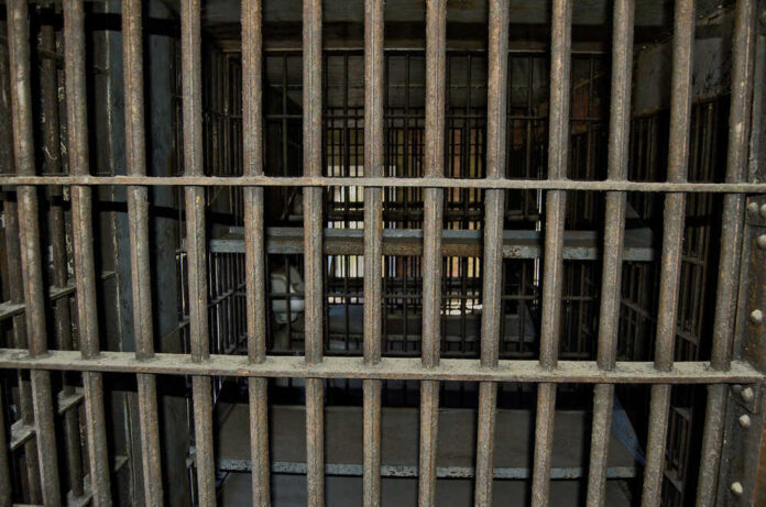 Empty, rusty barred jail cell with metal bunks.
