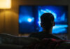 Movie Fan-Favorite Gone Person sitting on a couch watching a television screen in a dimly lit room
