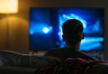Person sitting on a couch watching a television screen in a dimly lit room
