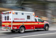 Evening Cast, Sudden Horror Red and white ambulance driving on a city street.
