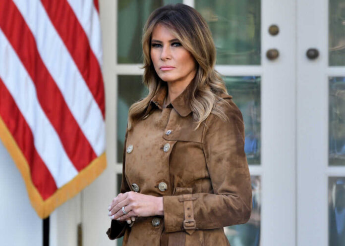 Melania Trump standing outdoors in a brown suede trench coat