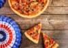 Pizza with slices on wooden table beside patriotic paper fans