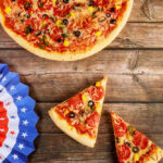 Pizza with slices on wooden table beside patriotic paper fans