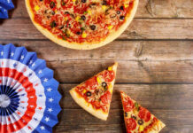 Pizza with slices on wooden table beside patriotic paper fans