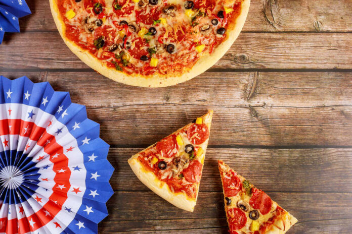 Pizza with slices on wooden table beside patriotic paper fans