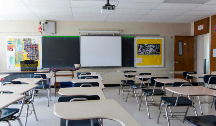 Empty classroom with desks, projector, and chalkboard.