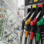 Fuel pump nozzles next to spread of U.S. hundred-dollar bills