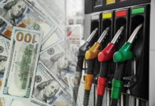 Fuel pump nozzles next to spread of U.S. hundred-dollar bills